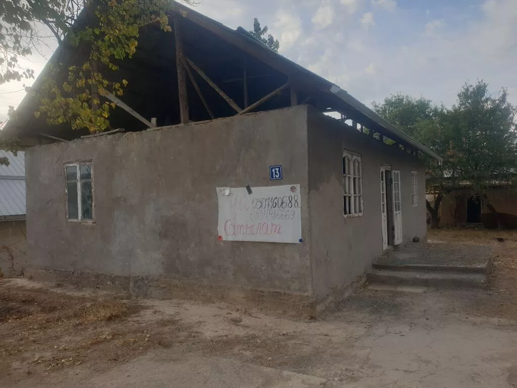 Одноэтажный дом с мансардной крышей на участке с деревьями. -